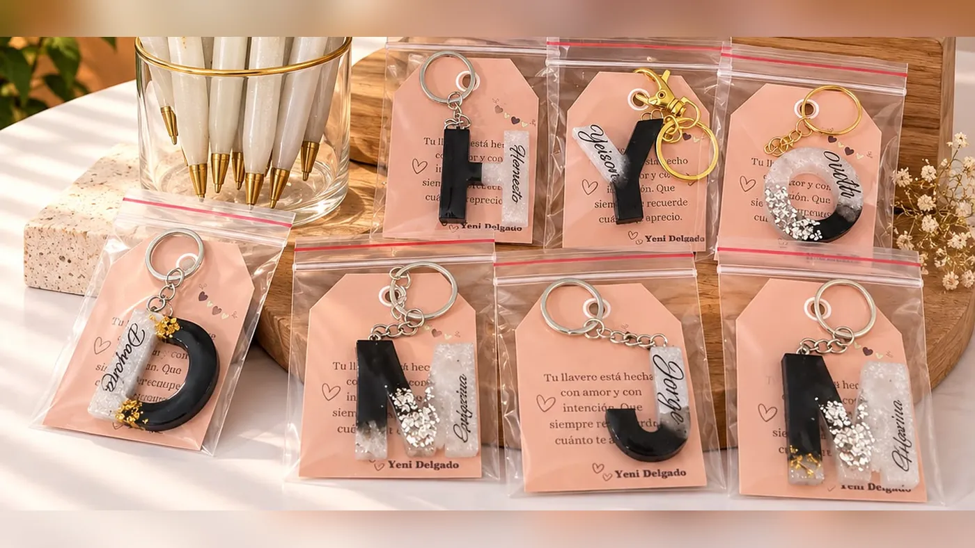 Seven black and white resin keychains with each person's initial and name, packed one by one with a message card, Detalles de Amor Medellín