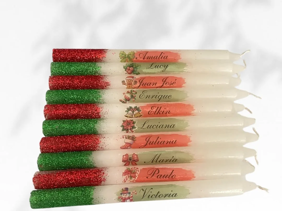 Ten personalized candles, each painted with a name over red and green glitter with Christmas motifs, made by Detalles de Amor in Medellín